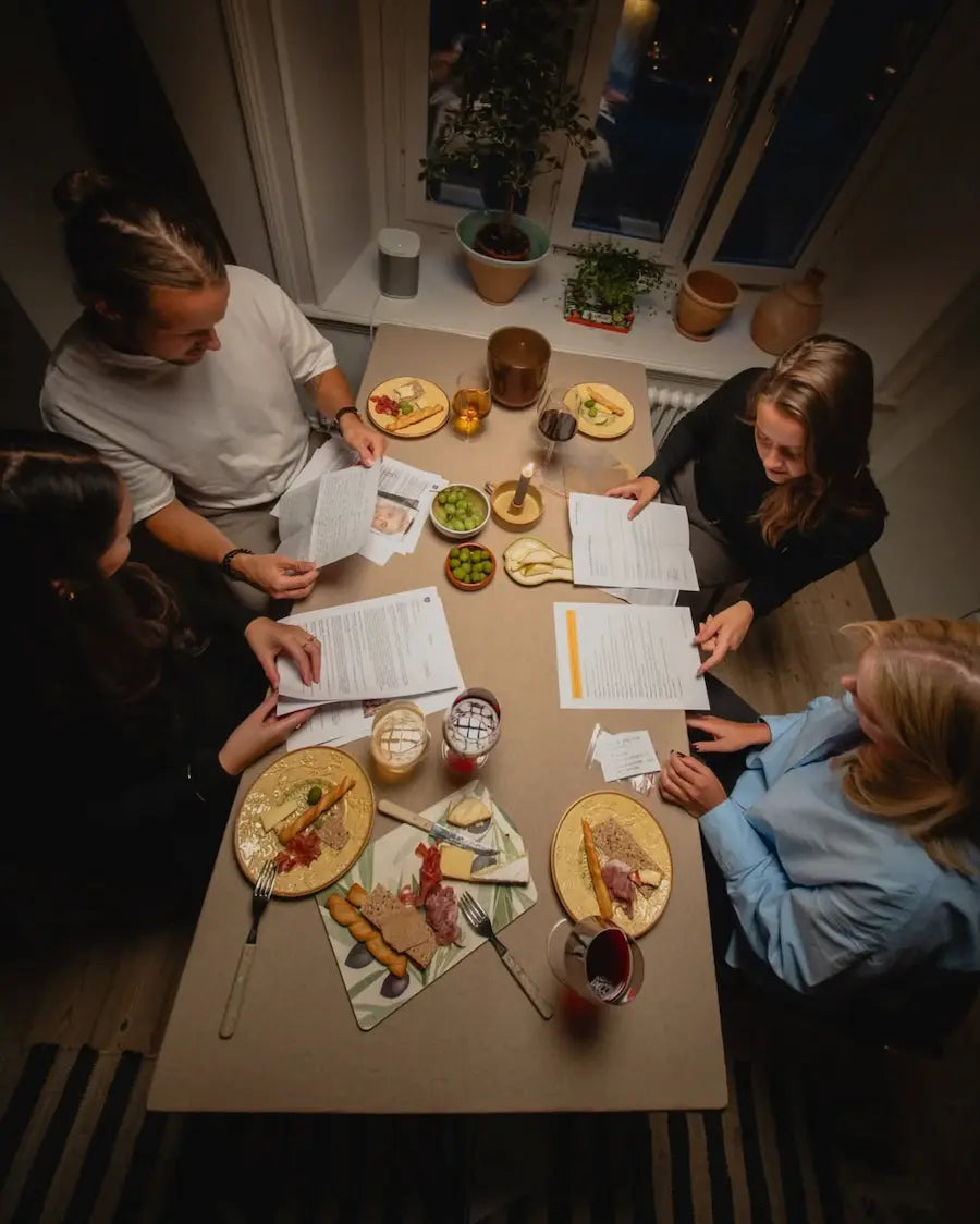 Fyra personer löser en mordgåta tillsammans runt ett bord med mat och dryck.
