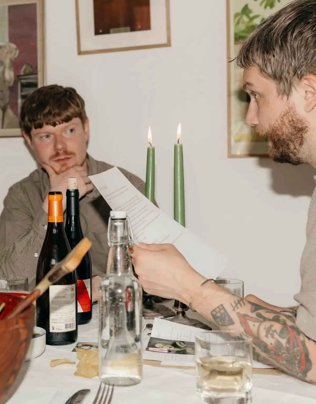 Två personer samtalar vid ett bord med spelmaterial, mat och dryck.